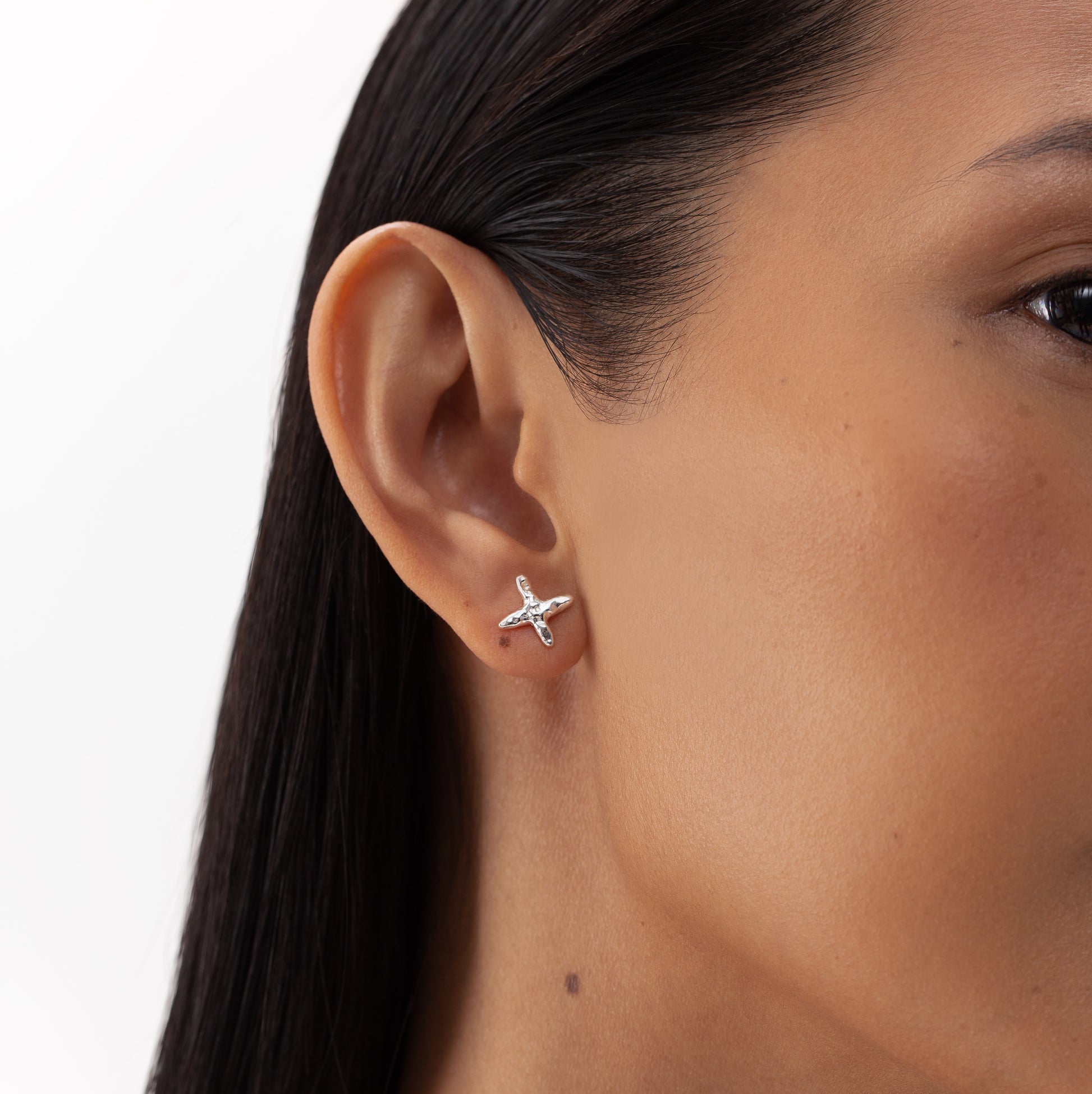 Close-up of a woman's ear with a silver Cross stud earring, showcasing ONEHE's sustainable, hypoallergenic design made from recycled sterling silver. Dimensions: 12 x 12mm.