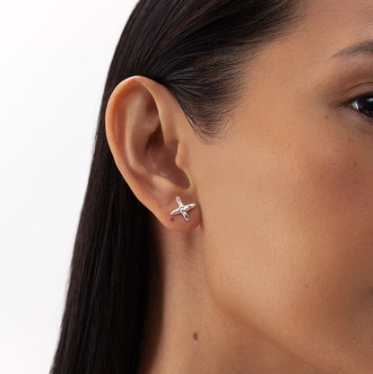 Close-up of a woman's ear with a silver Cross stud earring, showcasing ONEHE's sustainable, hypoallergenic design made from recycled sterling silver. Dimensions: 12 x 12mm.